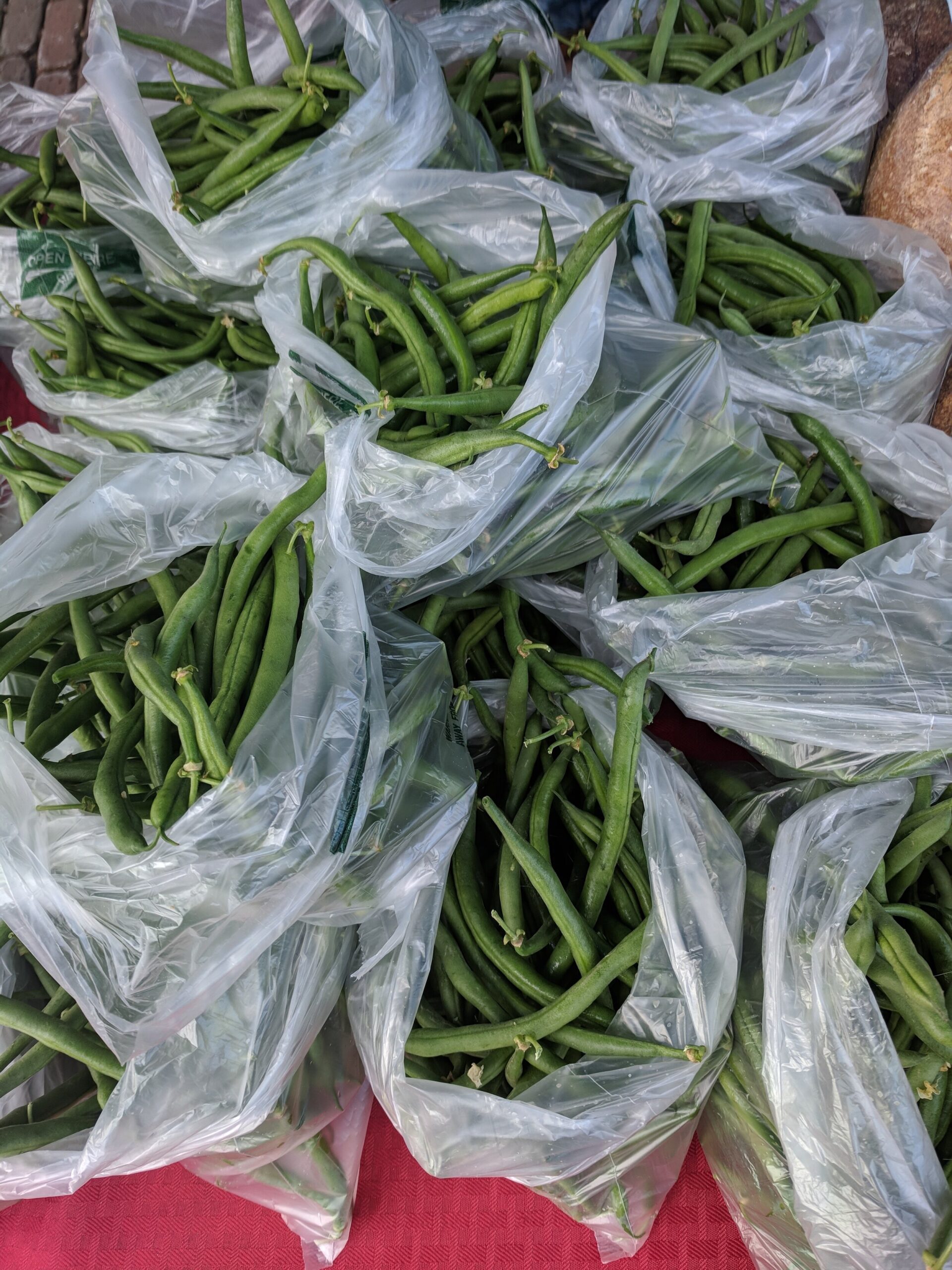 Fresh green beans in plastic bags stacked on a table at a farmers market, showcasing vibrant produce ready for sale.